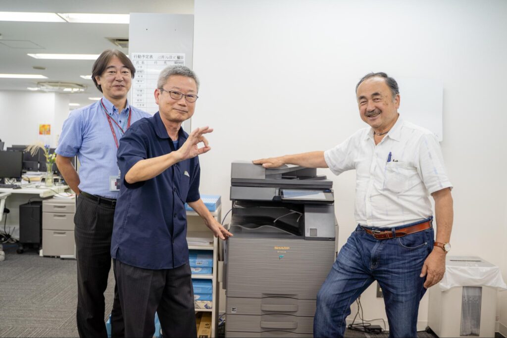 IBS営業担当、EnviX様・社員の豊島さん、中里代表取締役。複合機の使い心地を「OK」ポーズで表現していただいた。